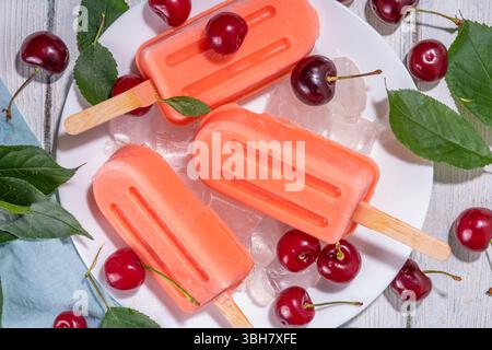 Kirschjoghurt Eiscreme Lollypops, hausgemachtes Beerenobst Eis mit frischen Kirschen, weißer Holzhintergrund Kopierbereich Stockfoto