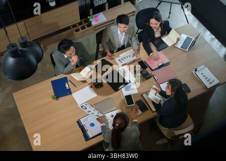 Eine Gruppe erwachsener asiatischer Geschäftsleute, die während einer Besprechung in einem modernen Büro zusammenarbeiten und Finanzberichte, Diagramme und Diagramme analysieren, um zu sehen Stockfoto