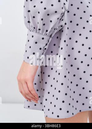 Gepunktete Kleidung mit schwarzen Punkten und geknöpften Bündchen. Neben dem Kleid liegt eine Hand, die eleganten Stoff und Design unterstreicht Stockfoto