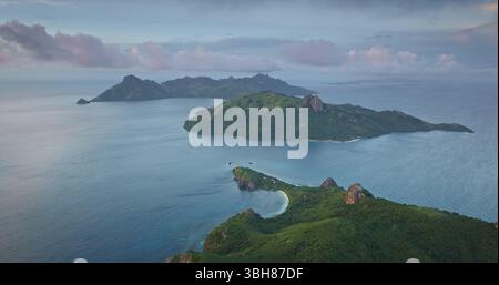 Aufnahmen von Luftaufnahmen der Fidschi-Inseln während des Sonnenuntergangs, mit üppigen grünen Hügeln, lebendigem türkisfarbenem Wasser und dramatischem Himmel voller rosa und grauer Wolken. Fantastischer Naturreisehintergrund Stockfoto