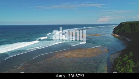 Atemberaubender Blick aus der Vogelperspektive mit sanften Wellen am Balangan Beach, einem beliebten Surfspot in Bali, Indonesien, mit kristallklarem türkisfarbenem Wasser unter einem blauen Himmel Stockfoto