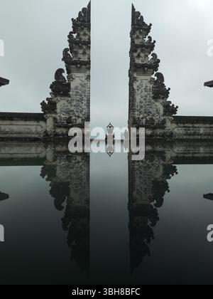 Frau meditiert, Tempeltore, Lagunenspiegelung. Eine Frau meditiert ruhig zwischen den ikonischen Toren des Lempuyang Tempels in Bali, ihre Silhouette mir Stockfoto