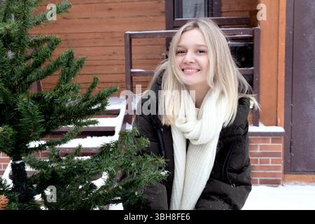 Eine junge blonde Frau schmückt im Winter einen Weihnachtsbaum draußen Stockfoto