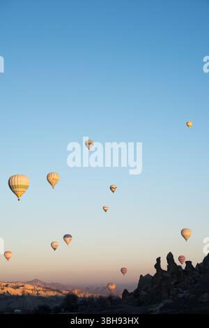Am frühen Morgen in Kappadokien fliegen farbenfrohe Heißluftballons über bezaubernde Felsformationen und bieten atemberaubende Ausblicke. Stockfoto