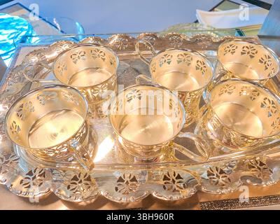 Goldtöne, klassischer Stil. Strukturierte Vintage-Gläser mit Goldton glänzen auf einer reflektierenden Schale, das Muster reflektiert das Licht, perfekt für stilvolle dr. Stockfoto
