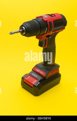 Vertikaler kompakter DIY-Schraubendreher platzt vor gelbem Hintergrund. Ergonomische Form und einfache Bedienelemente. Benutzerfreundliches schnurloses Werkzeug im Haushalt Stockfoto