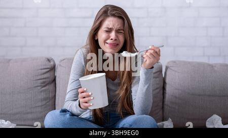 Emotionales Essen. Gestresste Frau weinte auf dem Sofa mit Eimer Eis, sah traurigen Film und Gefühl deprimiert Stockfoto