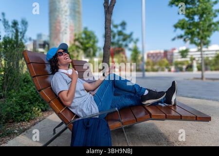 Glücklicher digitaler Nomad, der sich auf der Bank in barcelona entspannt und die Balance zwischen Arbeit und Freizeit genießt Stockfoto