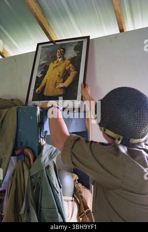 Eine Person in Militäruniform hängt ein gerahmtes Porträt von Adolf Hitler an eine Wand. Das Porträt ist in einem alten Holzrahmen. Weitere militärische Gegenstände sind VI Stockfoto