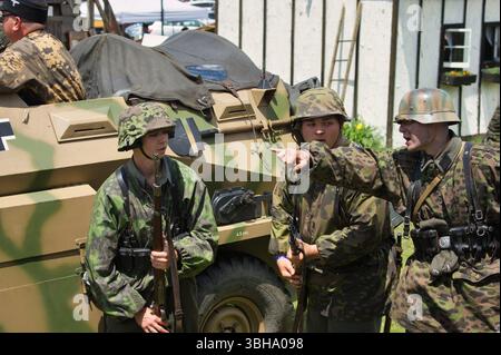 Drei Männer in deutschen Militäruniformen stehen in der Nähe einer SD.Kfz. 251 Halbbahn. Zwei Soldaten scheinen einen dritten zu unterrichten. Die Einstellung schlägt einen vor Stockfoto