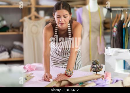 Die Schneiderin zeichnet in der Nähwerkstatt anhand von Mustern eine Skizze der zukünftigen Kleidung auf Papier Stockfoto