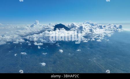Wolken schweben um den vulkanischen Gipfel und enthüllen die zerklüfteten Hänge und die satten grünen Wälder. Die Szene fängt die wilde Schönheit dieser tropischen Insel ein Stockfoto