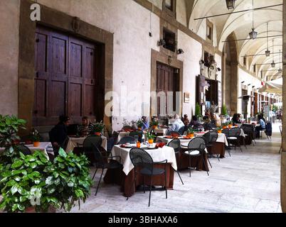 Restaurant im Freien, Sitzplätze unter überdachtem Bogengang mit dekorativen Pflanzen. Arezzo, Italien Stockfoto