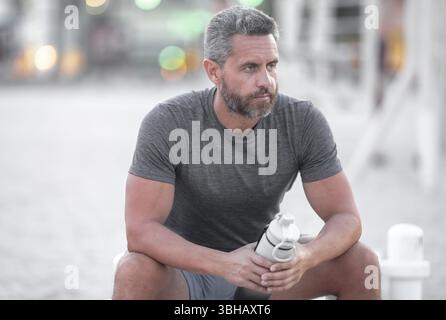 Sport-Fitness-Mann, der draußen auf einer Bank ruht. Reifes Fitnesssportmodell, das nach dem Training auf einer Bank sitzt. Hispanischer Sportmann macht danach eine Pause Stockfoto