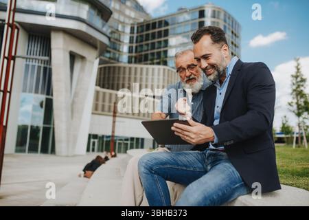 Vater und erwachsener Sohn teilen einen freudigen Moment, während sie etwas auf Tablet sehen. Stockfoto