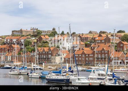 Whitby Hafen mit Yachten, die entlang des River Esk vertäut sind, roten Häusern und den Ruinen der Whitby Abbey auf East Cliff im Hintergrund. Stockfoto
