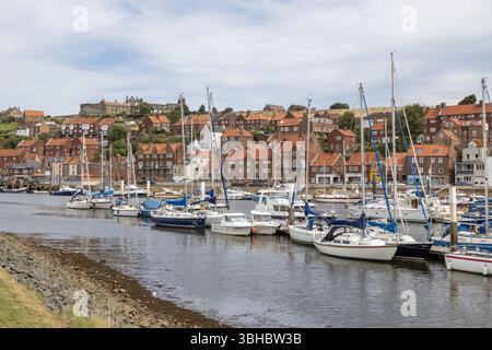 Whitby Hafen mit Yachten, die entlang des River Esk vertäut sind, roten Häusern und den Ruinen der Whitby Abbey auf East Cliff im Hintergrund. Stockfoto