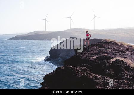 Die Läuferin hat eine Pause, während sie am Rande der Klippe am Meer steht Stockfoto