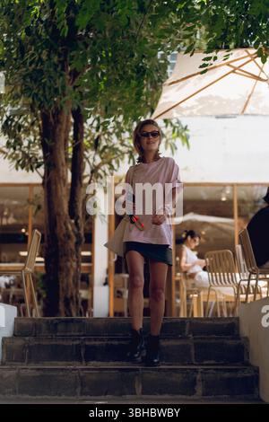 Frau, die draußen im legeren Outfit läuft, Sonnenbrille, selbstbewusster Vibe Stockfoto