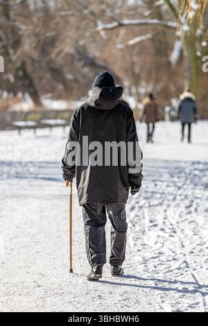 Ein älterer Herr mit Wanderstock spaziert durch den verschneiten Park Stockfoto