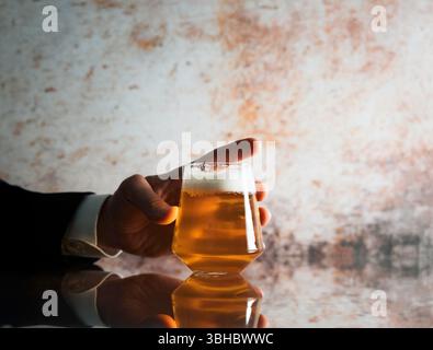 Mann in einem Anzug, der ein Bierglas auf einer reflektierenden Oberfläche hält Stockfoto