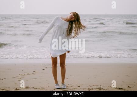 Fröhliche junge Frau, die an einem windigen Strandtag am Meer spielt Stockfoto