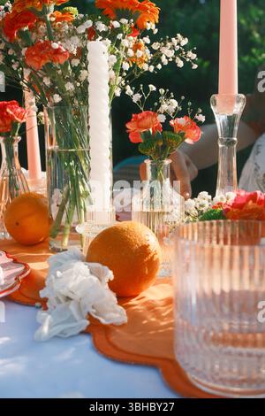 Tischplatte mit Orangen, Blumen, Kerzen und Gläsern in Sonnenschein Stockfoto