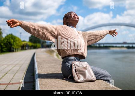 Fröhliche junge schwarze Frau, die den sonnigen Tag in der Stadt genießt. Stockfoto