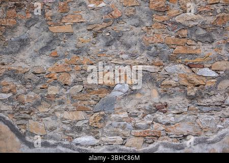 Alte schäbige Steinmauer mit Rissen. Der Putz ist abgestürzt und Steine und Ziegel freigelegt. Die Textur einer alten Steinmauer. Stockfoto