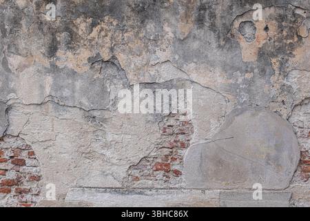 Alte schäbige Steinmauer mit Rissen. Der Putz ist abgestürzt und Steine und Ziegel freigelegt. Die Textur einer alten Steinmauer. Stockfoto