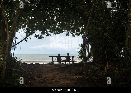 Silhoutte von Seniorenpaaren mit Blick auf das Meer auf einer Bank am Rande des Waldes des des Cahuita-Nationalparks, Costa Rica. Stockfoto