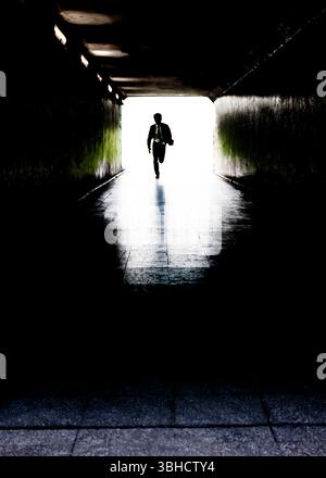 Ein Mann im Anzug läuft durch einen dunklen Tunnel zum Licht am Ende Stockfoto