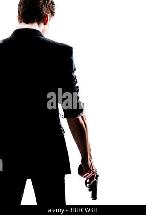 Ein Mann in einem Anzug, von hinten gesehen, hält einen Revolver an seiner Seite. Der helle weiße Hintergrund bildet seine Figur, schafft eine dramatische und aufsehenerregende Figur Stockfoto