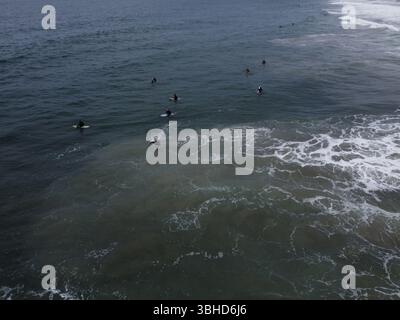 Aus der Vogelperspektive sehen Surfer, die in der Nähe des Manhattan Beach Pier unter stimmungsvollem Himmel Wellen fangen – Kaliforniens Küste in Bewegung von oben. Stockfoto