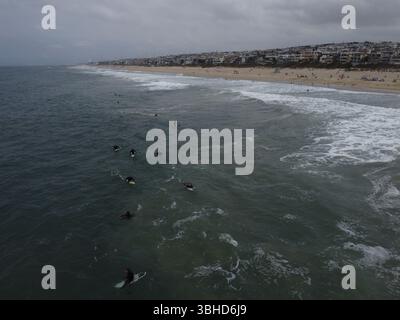 Aus der Vogelperspektive sehen Surfer, die in der Nähe des Manhattan Beach Pier unter stimmungsvollem Himmel Wellen fangen – Kaliforniens Küste in Bewegung von oben. Stockfoto