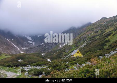 Abgelegene Berghütte in malerischer Hochlandlandschaft mit sanften Hügeln und dramatischer felsiger Bergkulisse Stockfoto