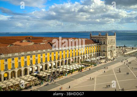 Große Aufnahme des Commerce Square oder Praca do Comercio in Lissabon, Portugal, mit der berühmten gelben Pombaline-Architektur, belebten Cafés im Freien, dem Fluss Tejo, dem Stadtleben, der historischen Innenstadt, sonniger Tag, Himmel mit Wolken. Sommerurlaub, Reiseziel Stockfoto