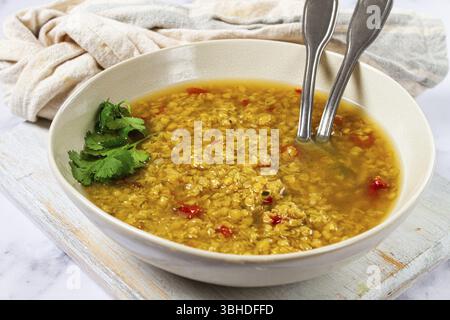 Eine warme Linsensuppe in kräftiger goldener Farbe wird in einer rustikalen Schüssel serviert. Die Suppe enthält frische Kräuter und Gewürze, was sie zu einem köstlichen Gericht macht Stockfoto