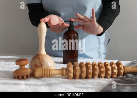 Weibliche Massagetherapeutin in professioneller Uniform Putting Lotion , und Organisieren von hölzernen Massagewerkzeugen, wie Rollen, auf einem Massagetisch in einer ruhigen B Stockfoto