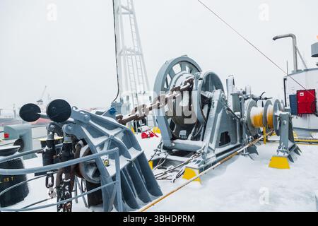 Das Anlegedeck eines Frachtschiffes mit Ankerwinden, einer Ankerkette an Winden, Pollern und Haws mit Anlegeseilen, gefroren und mit Schnee bedeckt. Sn Stockfoto