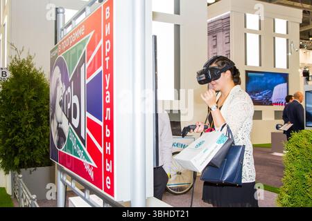moskau, russland, 28.06.2017 Eine Frau trägt ein Virtual-Reality-Headset und schaut sich ein Schild an. Das Schild ist auf Russisch und hat ein farbenfrohes Design Stockfoto