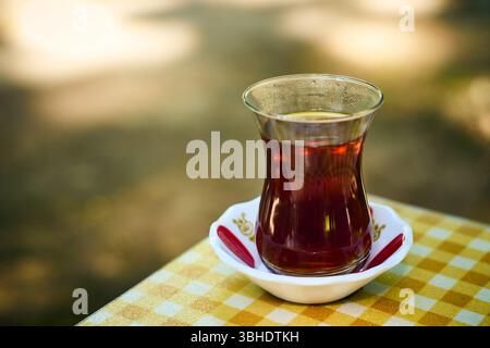 Eine Nahaufnahme aromatischen schwarzen Tees in einem klassischen Armudu-Glas auf einer hellen karierten Tischdecke. Stockfoto