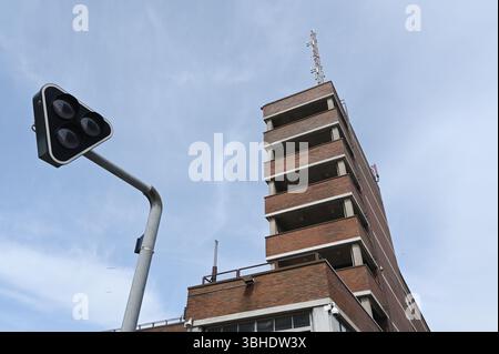 Eine beeindruckende Aufwärtsperspektive eines roten Backsteinhochhauses mit minimalistischer modernistischer Architektur, die mit einem einzigartigen dreieckigen Verkehrsli verglichen wird Stockfoto
