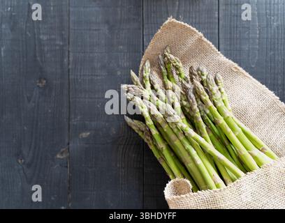 Top-down-Nahaufnahme von frischem grünem Spargel, teilweise mit rustikalem Sacktuch umwickelt Stockfoto