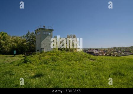 Hötensleben, Deutschland 27. April 2025: Im Bild: Dieses Bild zeigt einen der authentischen Wachtürme am Grenzdenkmal Hötensleben in Sachsen-Anhalt, einer der besterhaltenen Gedenkstätten der ehemaligen innerdeutschen Grenze. Der Turm steht auf einer erhöhten Beobachtungsposition, umgeben von grüner Landschaft und Bäumen, mit dem Blick auf die ehemalige Grenzregion und das angrenzende Dorf Hötensleben. Er symbolisiert die permanente Grenzüberwachung und die Absicherung der DDR-Grenze durch die Grenzsoldaten während des Kalten Krieges. Als Teil des umfassenden Grenzsicherungssystems war der WAC Stockfoto