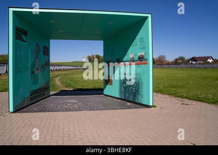 Hötensleben, Deutschland 27. April 2025: Im Bild: Dieses Bild zeigt einen zentralen Informationsbogen am Grenzdenkmal Hötensleben in Sachsen-Anhalt, einer der authentischsten und besterhaltenen Gedenkstätten der ehemaligen innerdeutschen Grenze. Der große, türkisblaue Bogen ist beidseitig mit Texten, Karten und historische Fotografien gestaltet, die Grenzregime der DDR detailliert erläutert, einschließlich der Grenzüberwachung, des Kontrollstreifens und der Grenzsoldaten. Im Hintergrund sind Elemente der originalen Grenzanlagen wie die Grenzmauer und ein Wachturm sichtbar, was die Inhalte Stockfoto