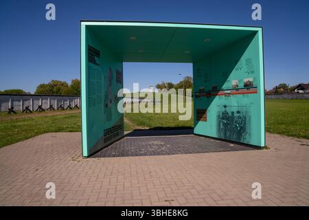 Hötensleben, Deutschland 27. April 2025: Im Bild: Dieses Bild zeigt den markanten Informationsbogen zum Thema Grenzregime am Grenzdenkmal Hötensleben in Sachsen-Anhalt, einer der authentischsten und besterhaltenen Gedenkstätten der ehemaligen innerdeutschen Grenze. Der große, türkisblaue Bogen präsentiert Texte, Karten und historische Fotografien, das Grenzsystem der DDR umfassend erläutert. Im Hintergrund bietet sich ein weiter Blick auf die originalen Grenzanlagen, darunter die charakteristische Grenzmauer Betonsegmente, Panzersperren Tschechenigel und der weit entfernte Wachturm, der Stockfoto
