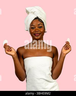 Happy Woman in Handtuch gewickelt mit Wattepads für die Hautpflege, um Schönheit und Selbstpflege zu fördern Stockfoto