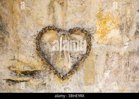 Weidenherz mit Band, das an einer alten Steinmauer hängt. Rustikale Romantik, handgemachter Charme und dekoratives Symbol auf dem Land. Stockfoto