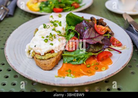 Ein gesundes Gourmet-Frühstück mit pochierten Eiern auf Avocadotoast, Lachs und frischem Salat Stockfoto